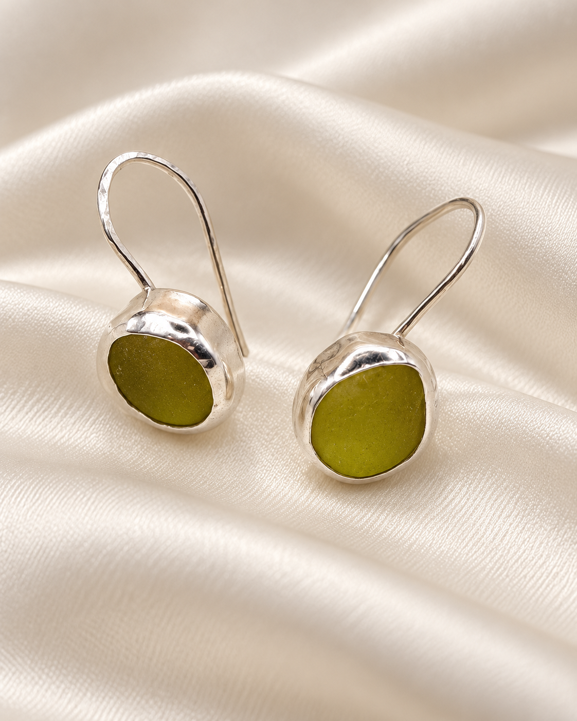 Handmade sterling silver Mira drop earrings set with green sea glass on ivory satin.