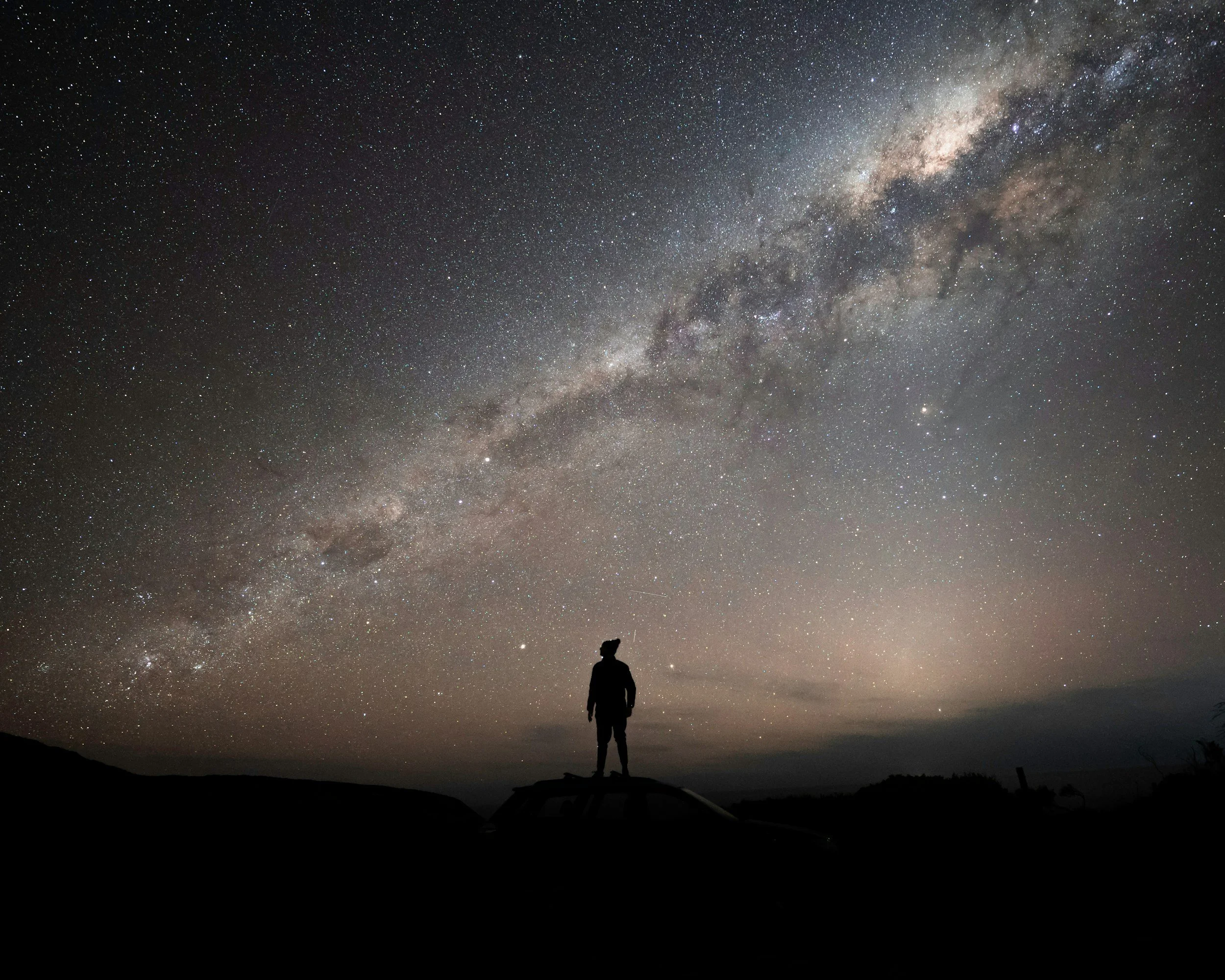 Person standing outdoors at night under a star-filled sky, with the Milky Way galaxy visible above.