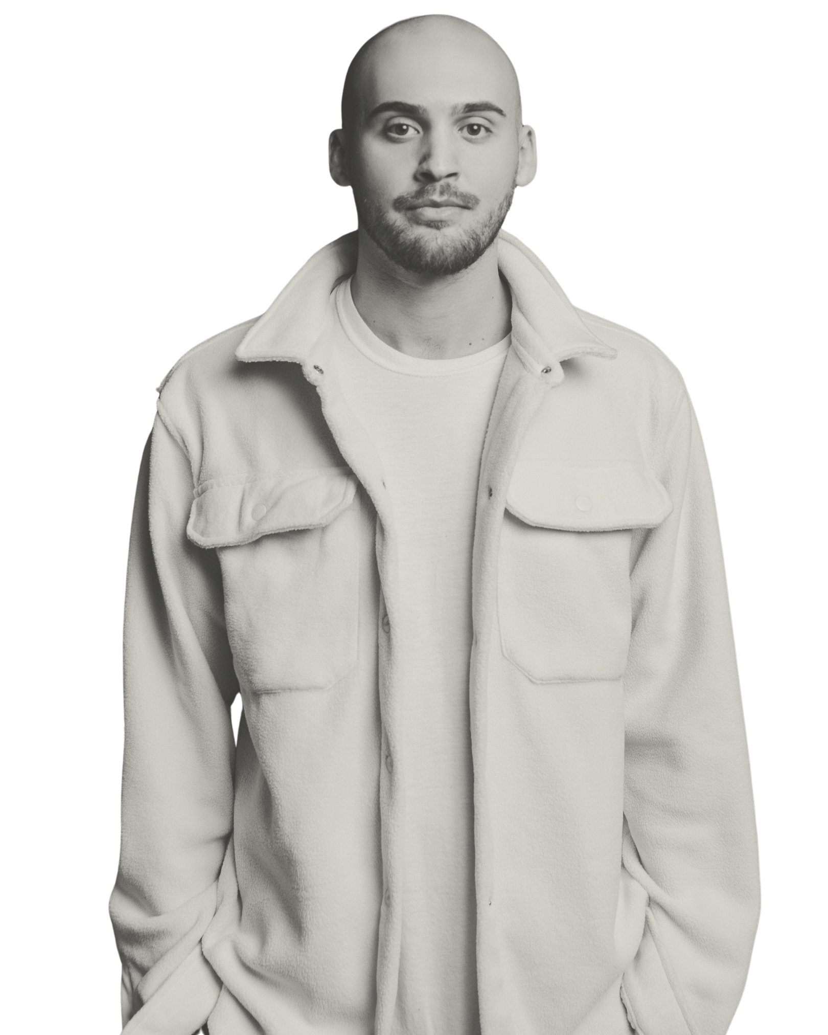 Black and white portrait of a man with a shaved head, beard, and mustache, wearing a light-colored fleece jacket over a T-shirt, standing against a black background.
