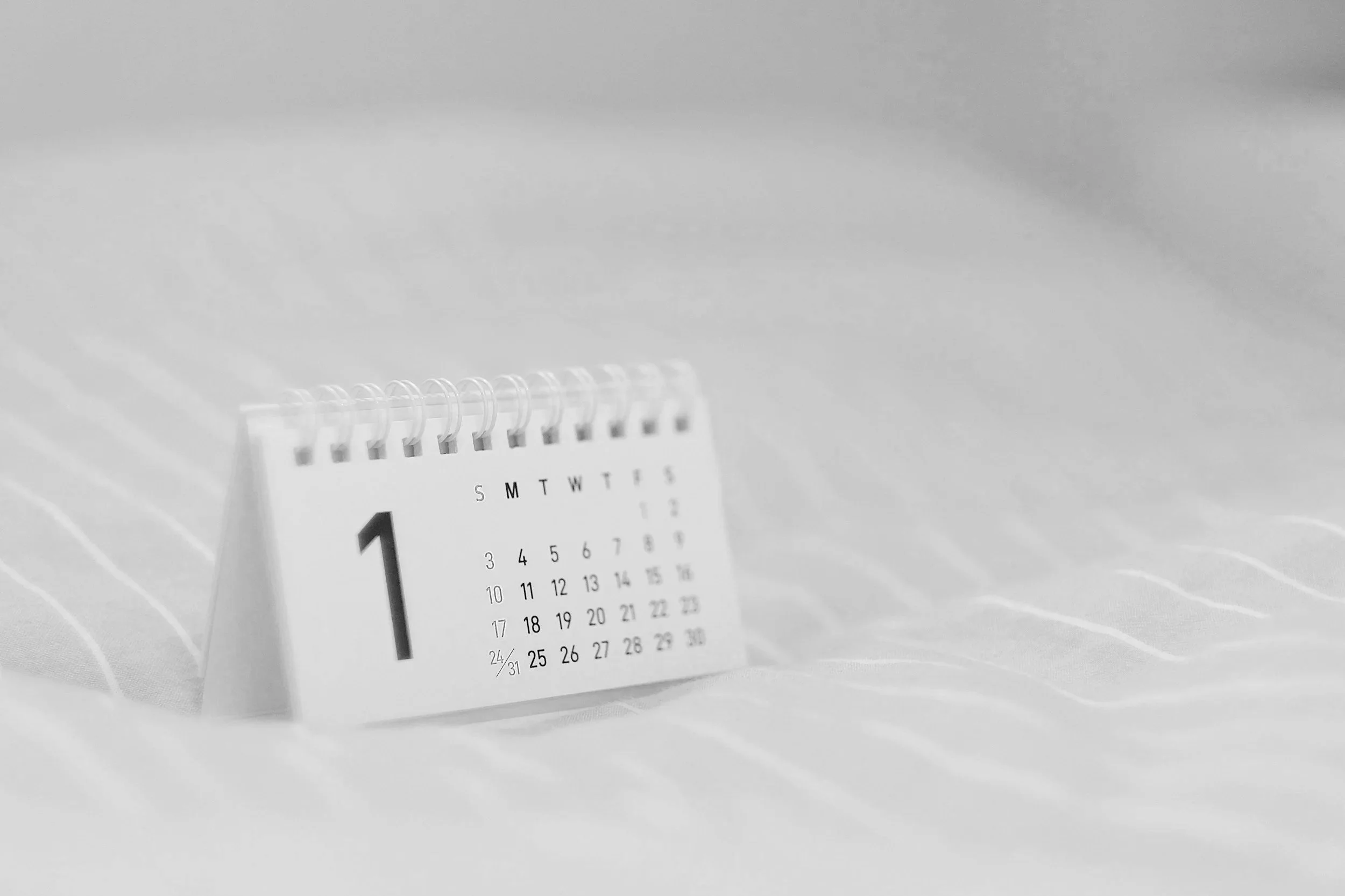 A spiral-bound desk calendar displaying the month of January with dates and days of the week visible, placed on a white surface.
