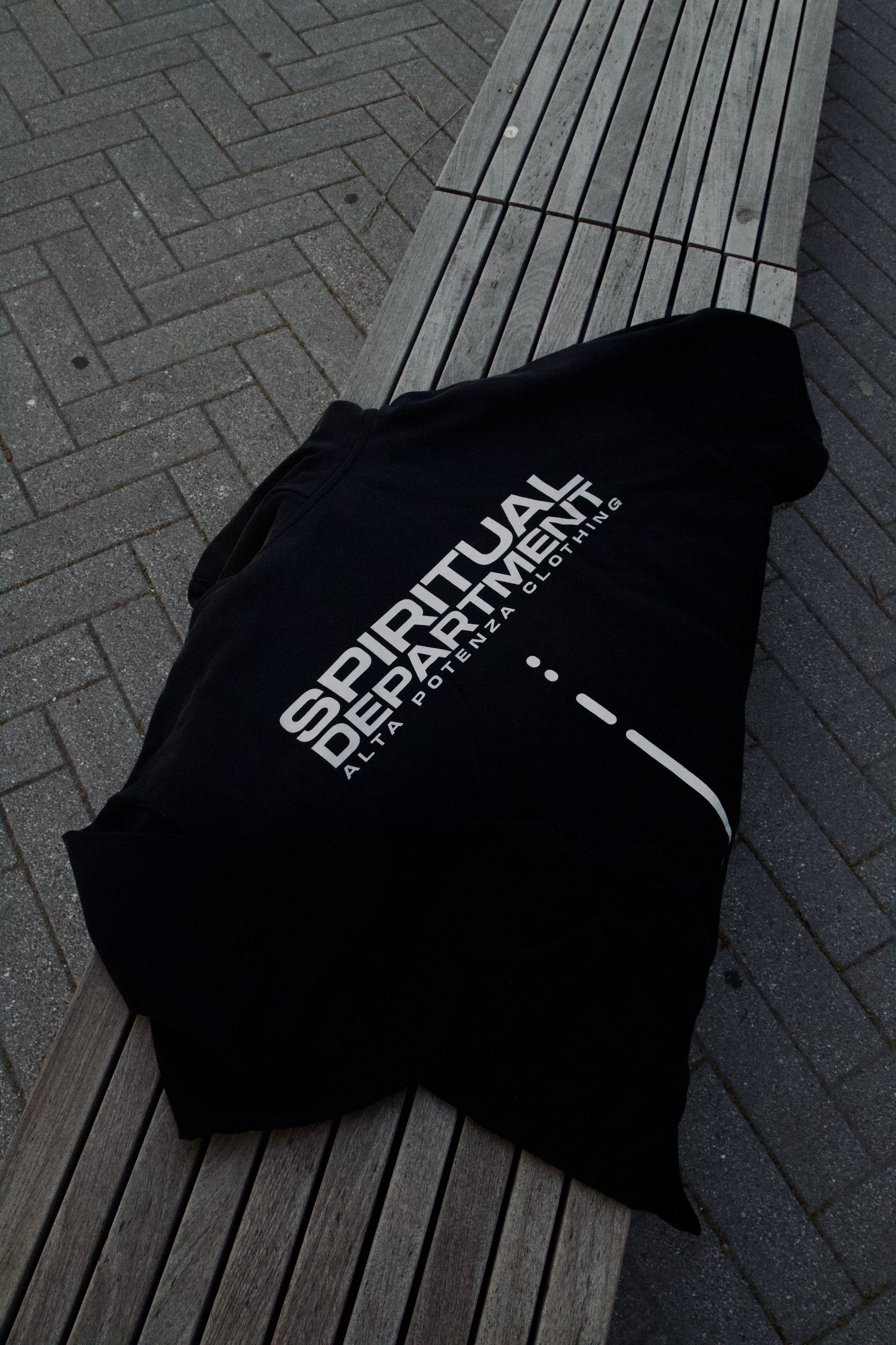 A black piece of clothing with white text lying on a wooden park bench.