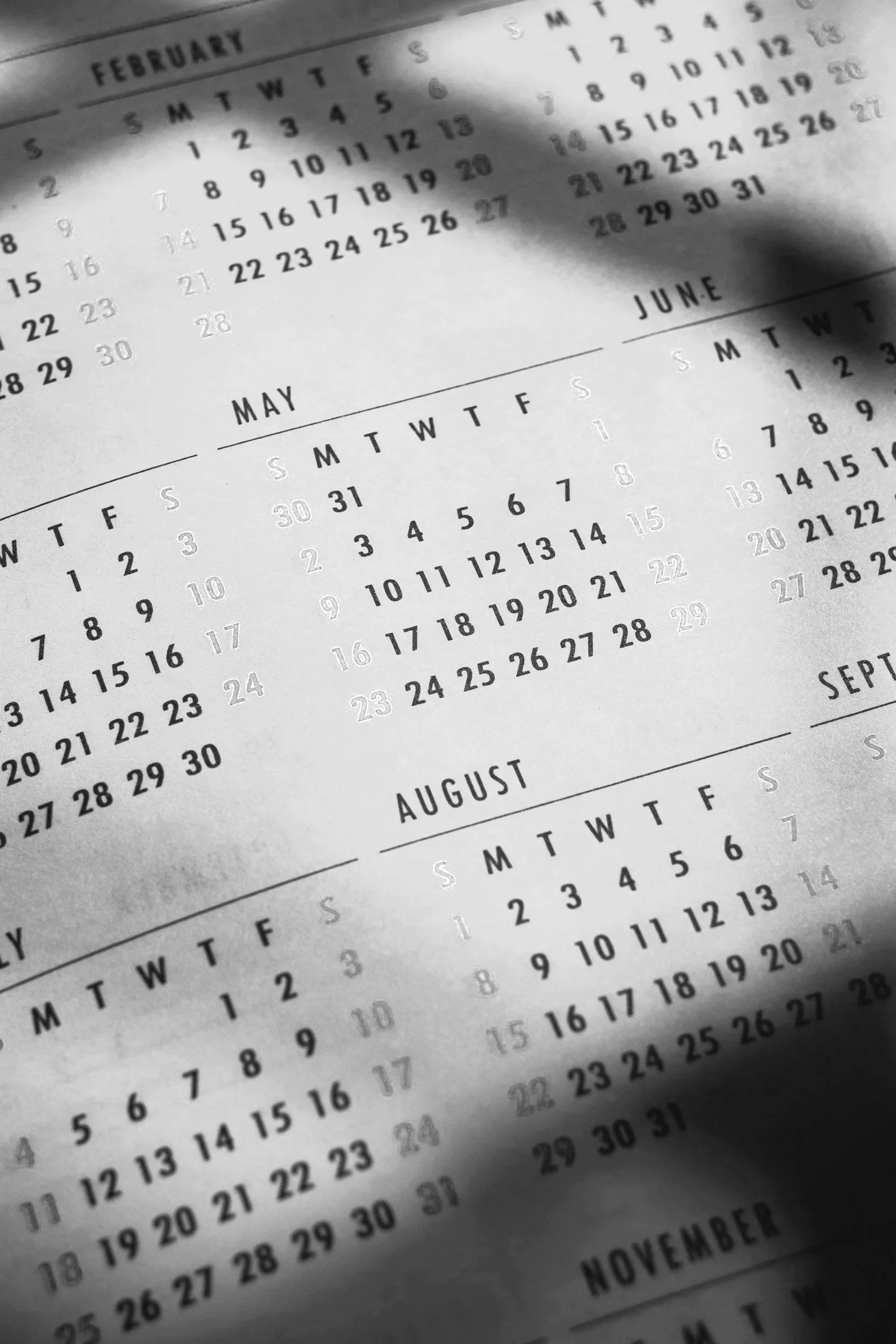 Close-up of a black-and-white paper calendar displaying February, May, June, August, September, October, November, and December months, with days arranged in a grid.