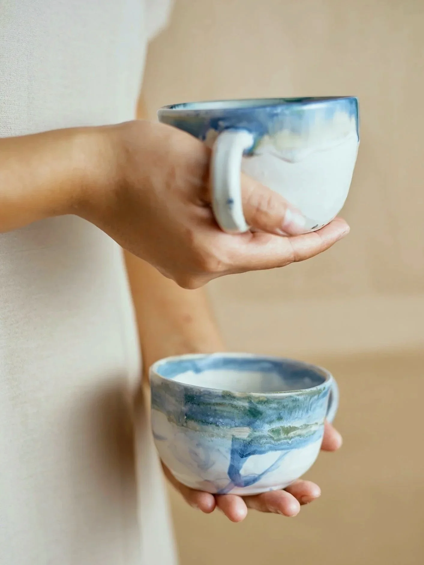 Person holding a ceramic bowl, pouring a cup of tea into it with a beige background.