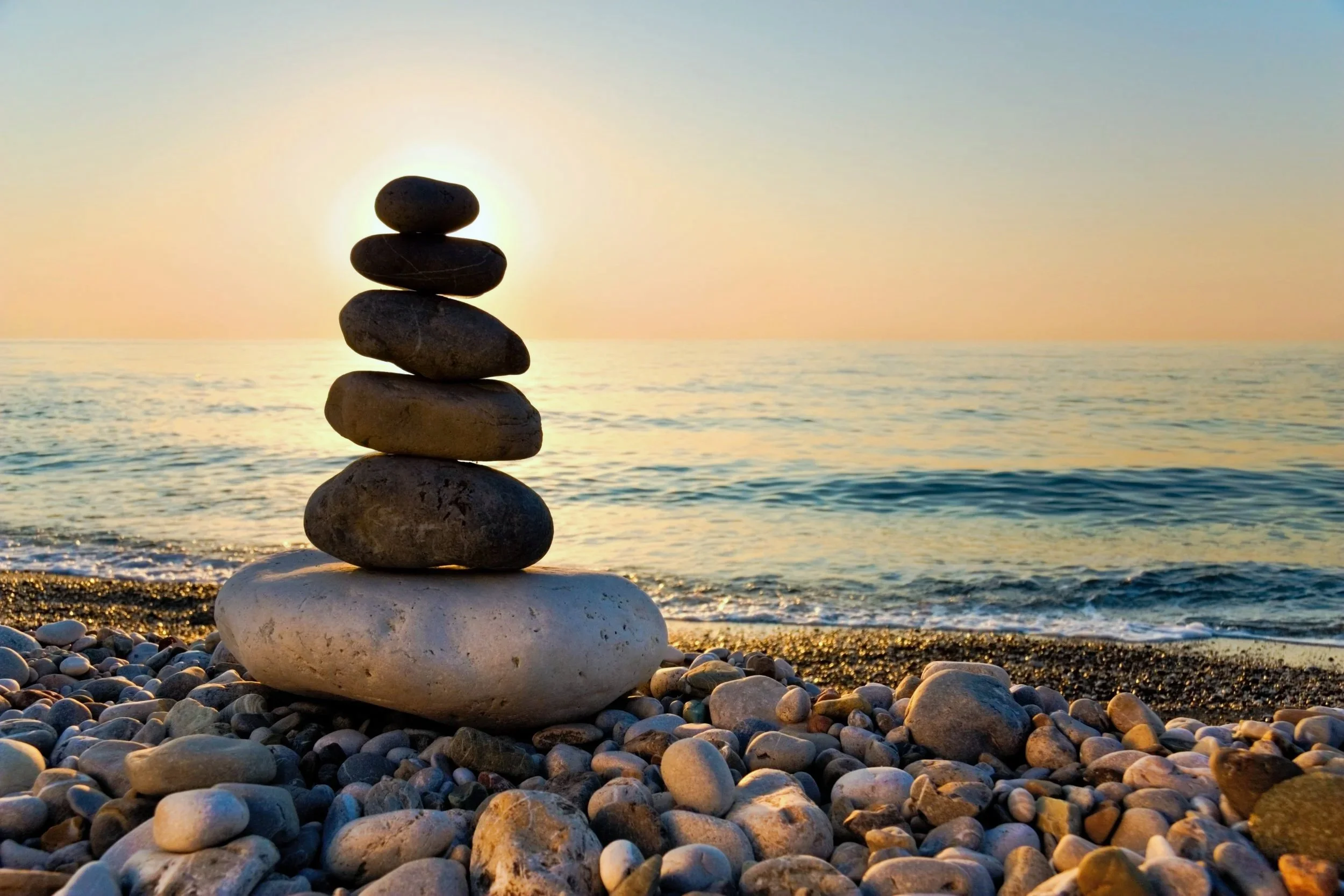 Stacked rocks on a beach with the setting sun in the background over the ocean