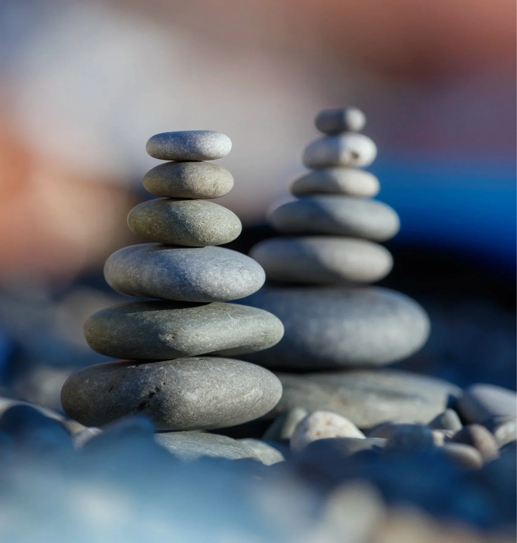 Close-up of stacked smooth, gray stones on the beach with a blurred background of sky and water.