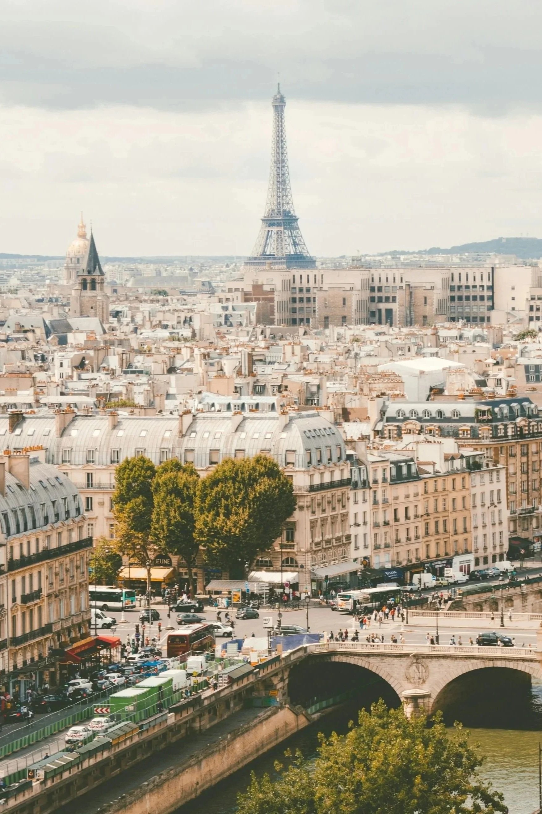 A cityscape with the Eiffel Tower in Paris, France, visible in the background. The photo shows buildings, a bridge, and a busy street with cars and pedestrians.