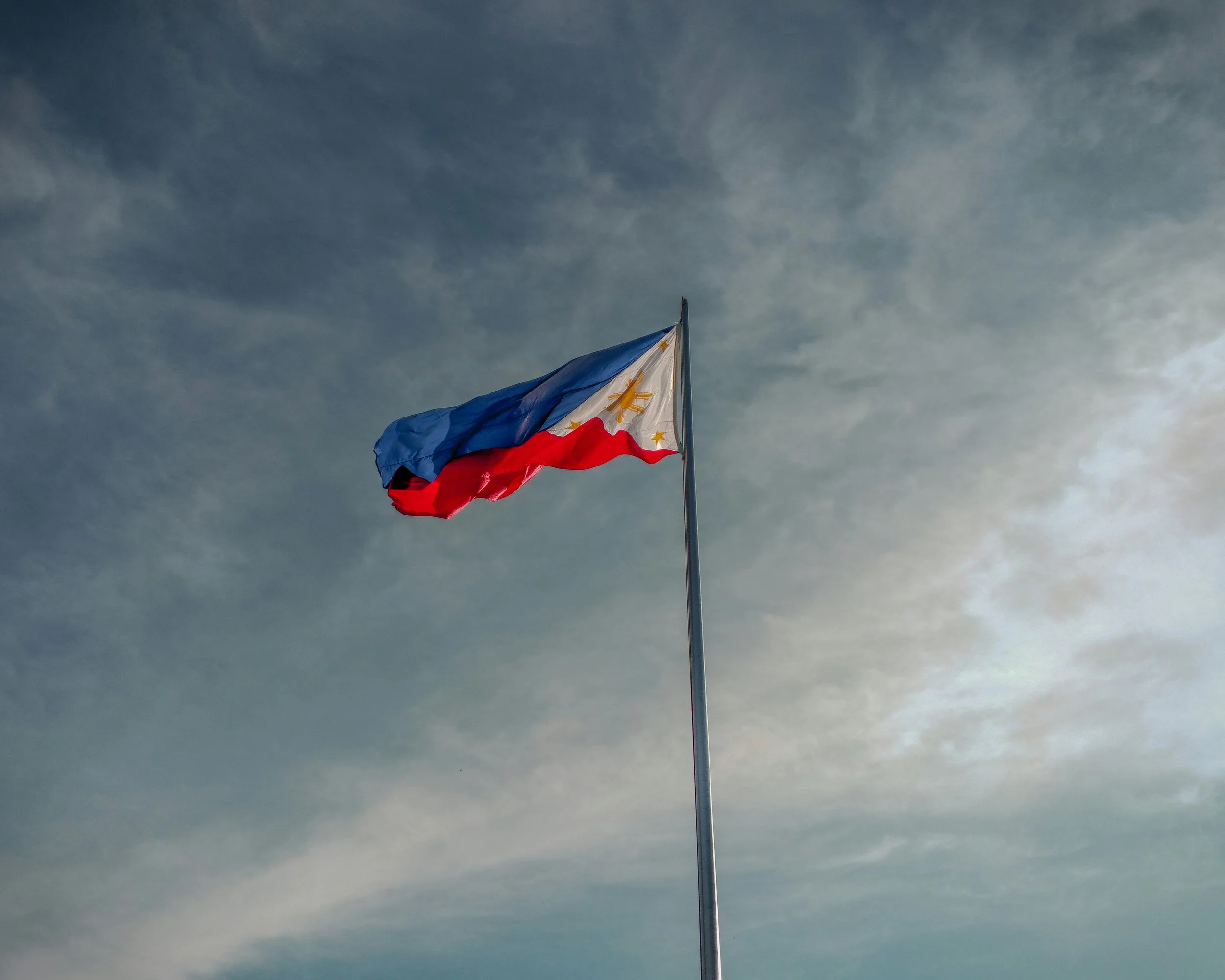A Filipino flag waving against a cloudy sky.