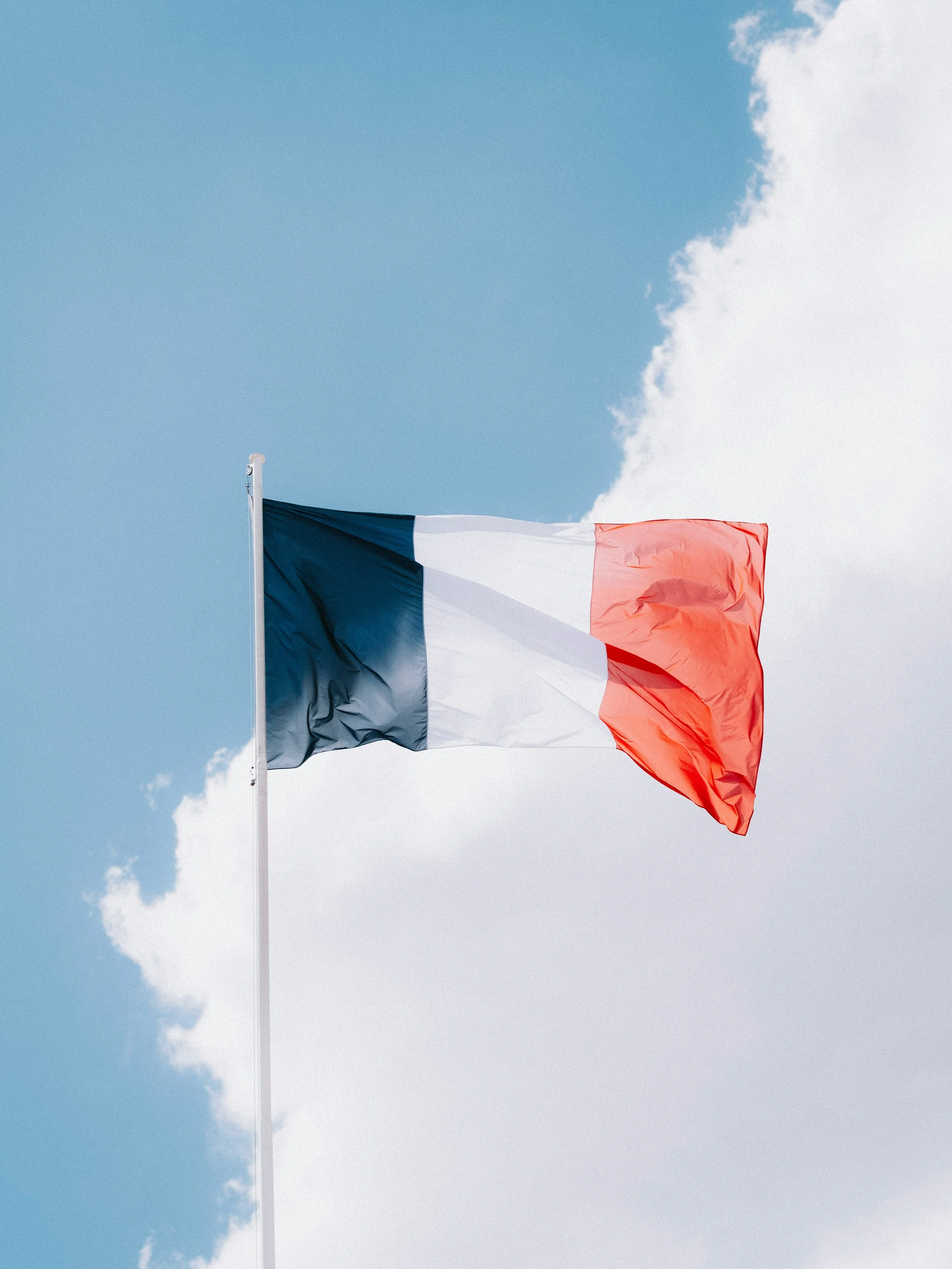 French flag waving against a partly cloudy sky.