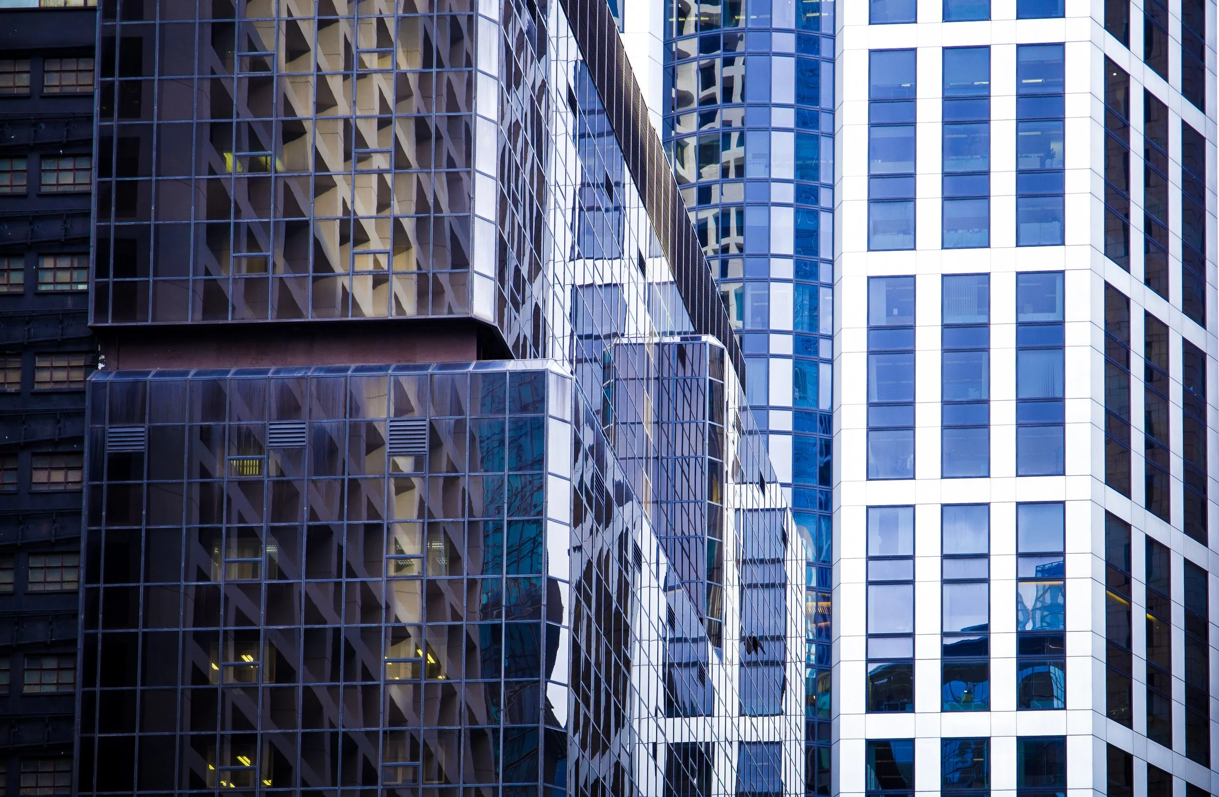 Close-up view of modern high-rise office buildings with glass facades reflecting other buildings in a city.