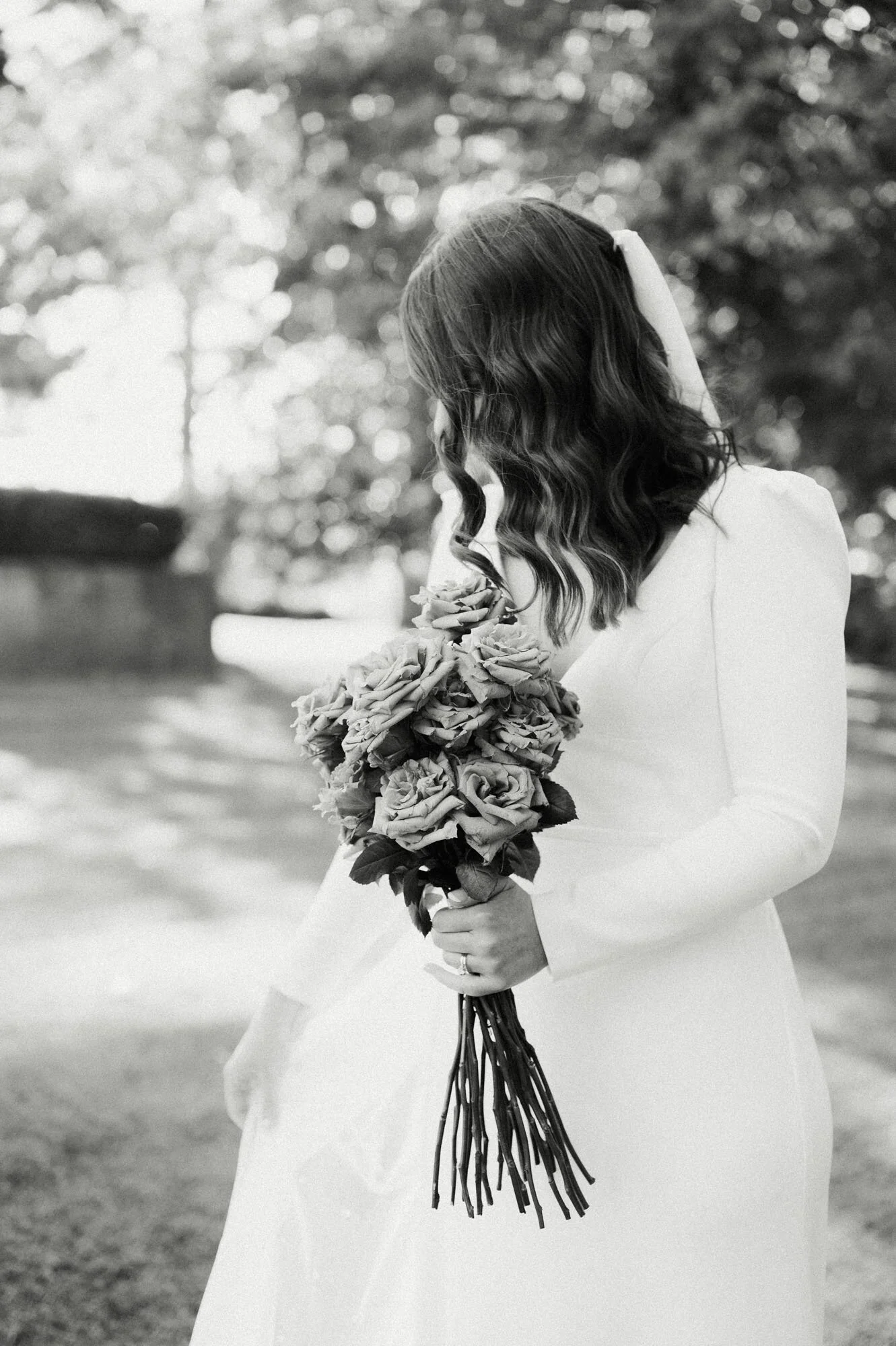 A woman in a white wedding dress holding a bouquet of roses outdoors.