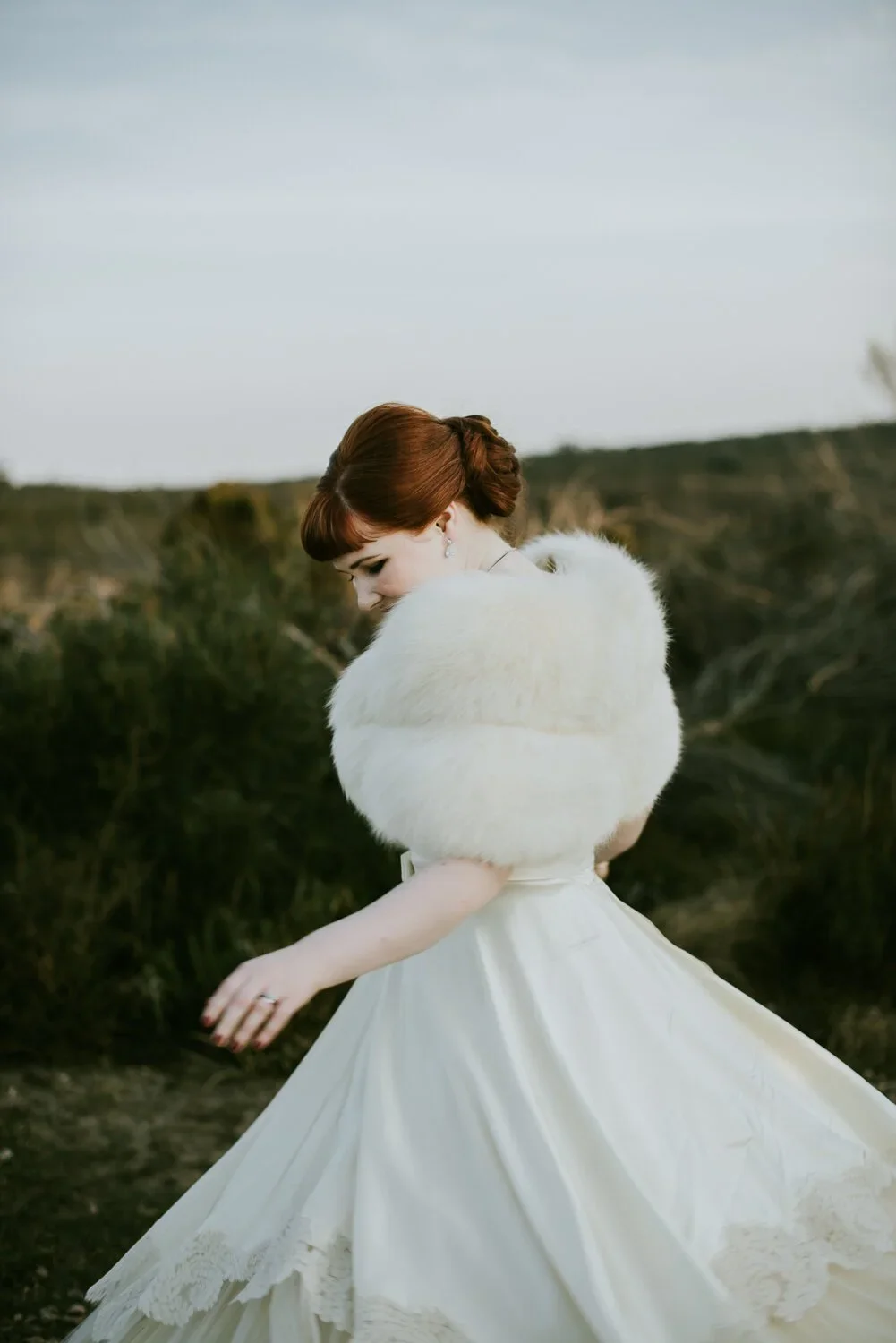 A woman in a white dress with a fluffy shawl outdoors in a field.