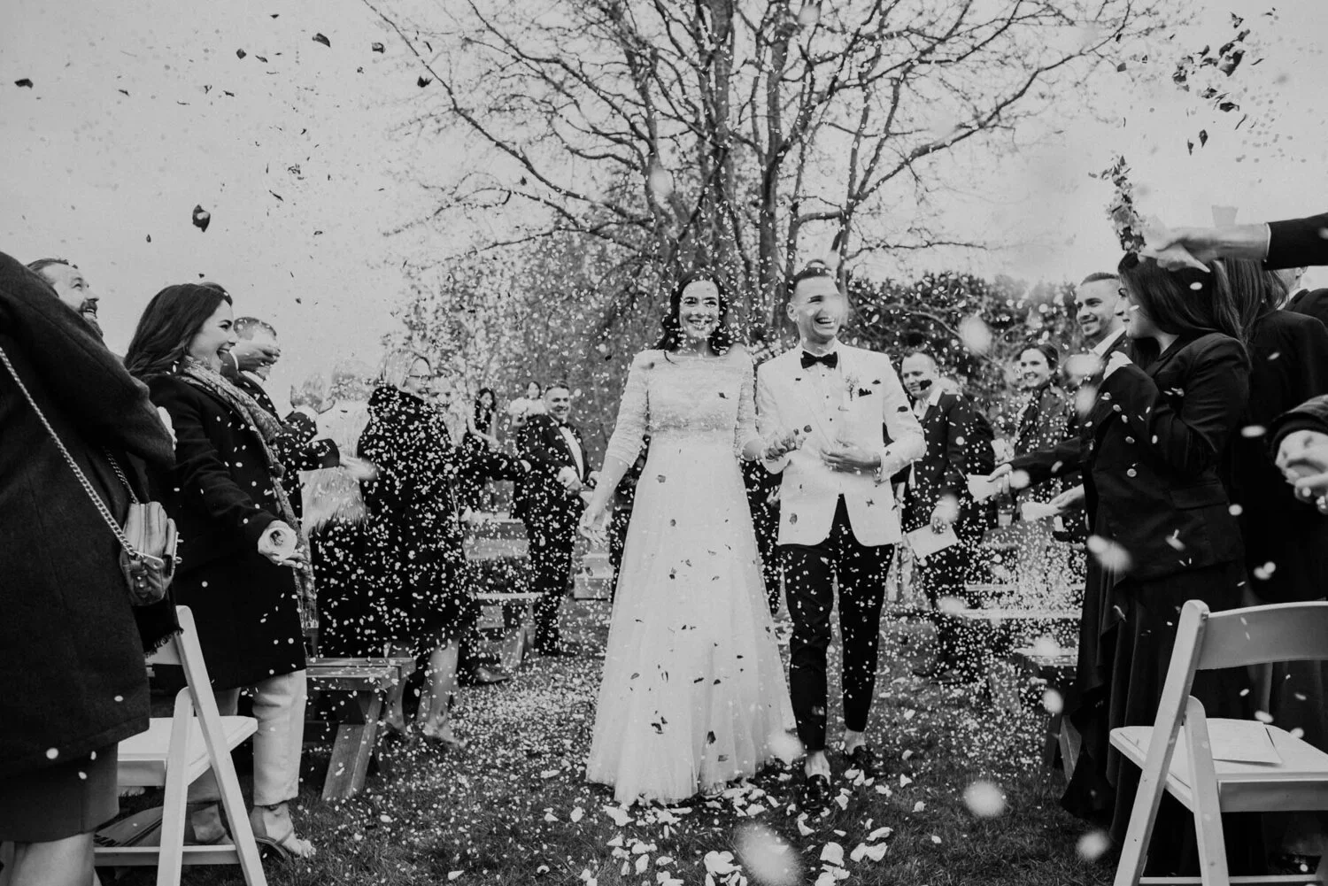 A wedding celebration with a bride and groom walking through a confetti parade outside, surrounded by guests.