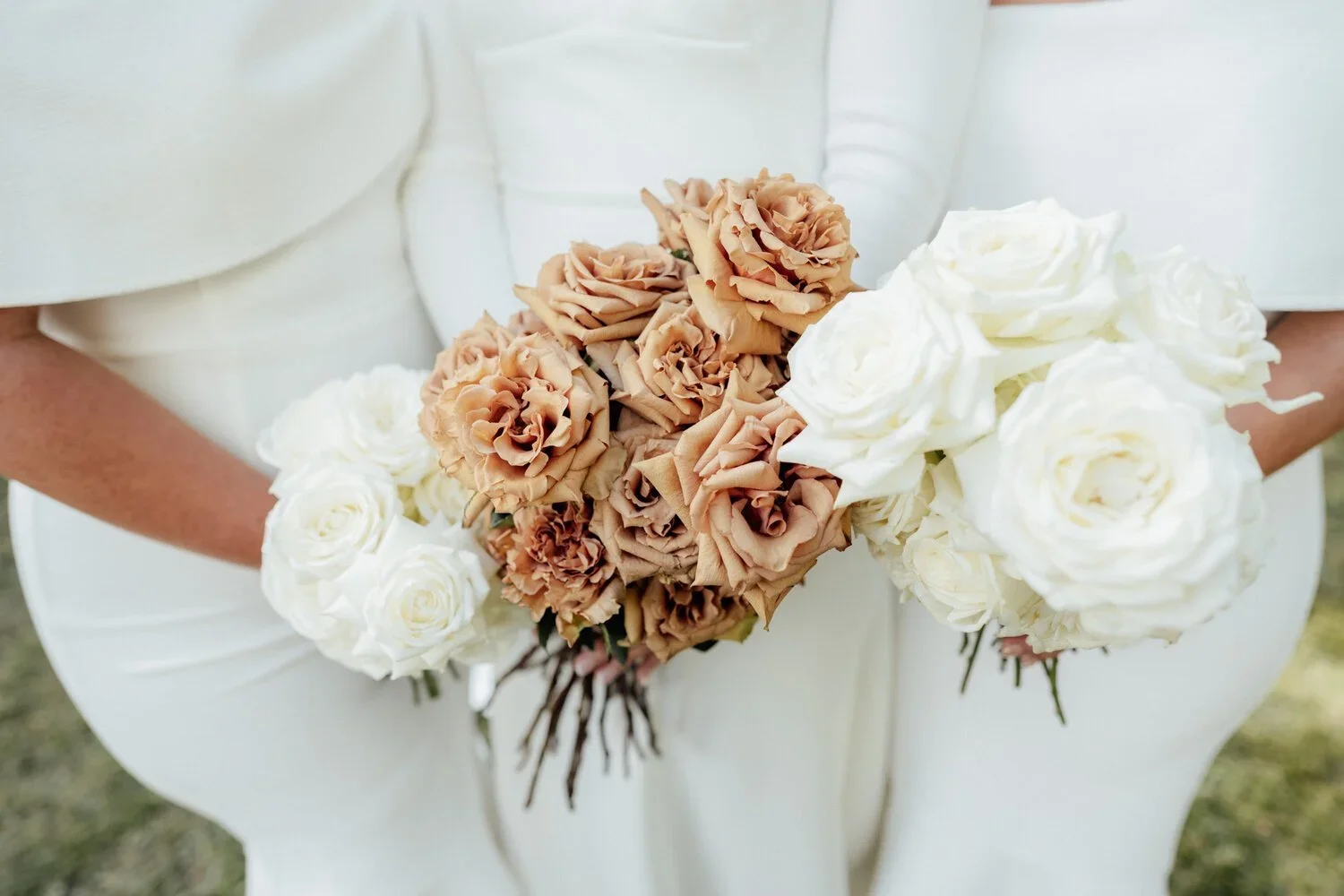 A person in a white dress holding a bouquet of white and beige roses.