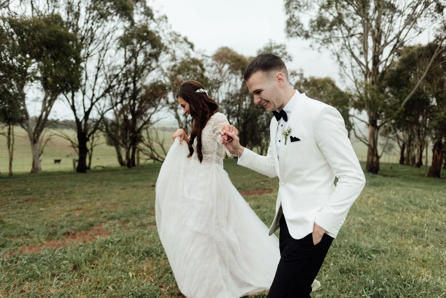 A bride and groom dancing outdoors on grass, with trees in the background, during what appears to be a wedding celebration.