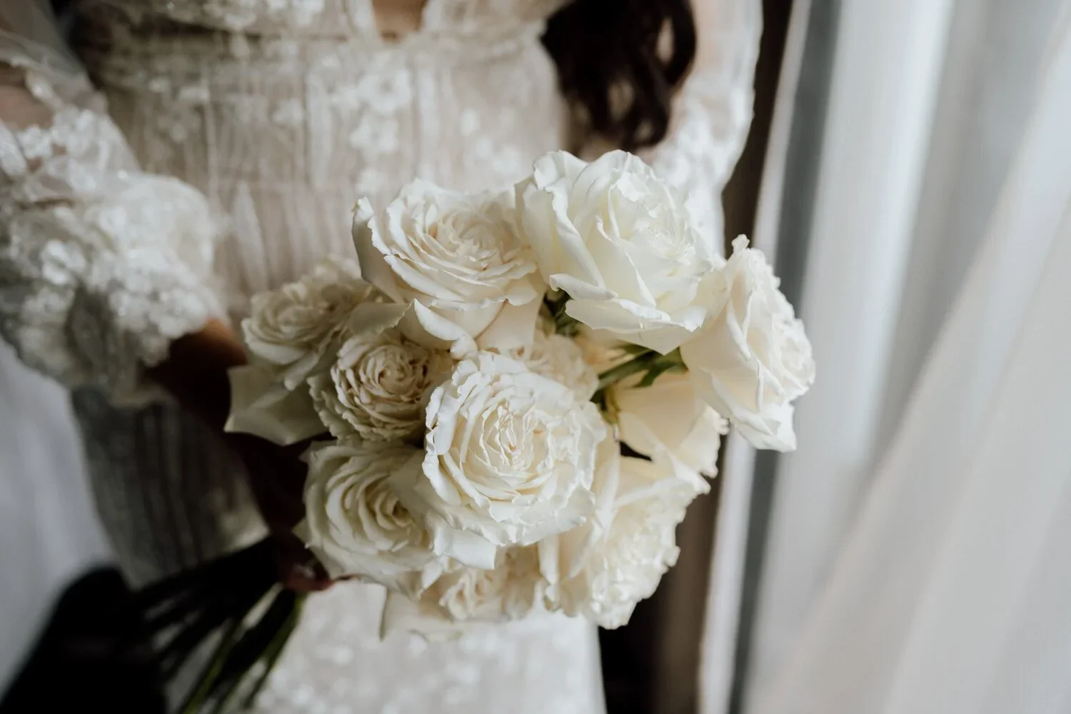 A bride holding a bouquet of cream-colored roses and peonies on her wedding day.