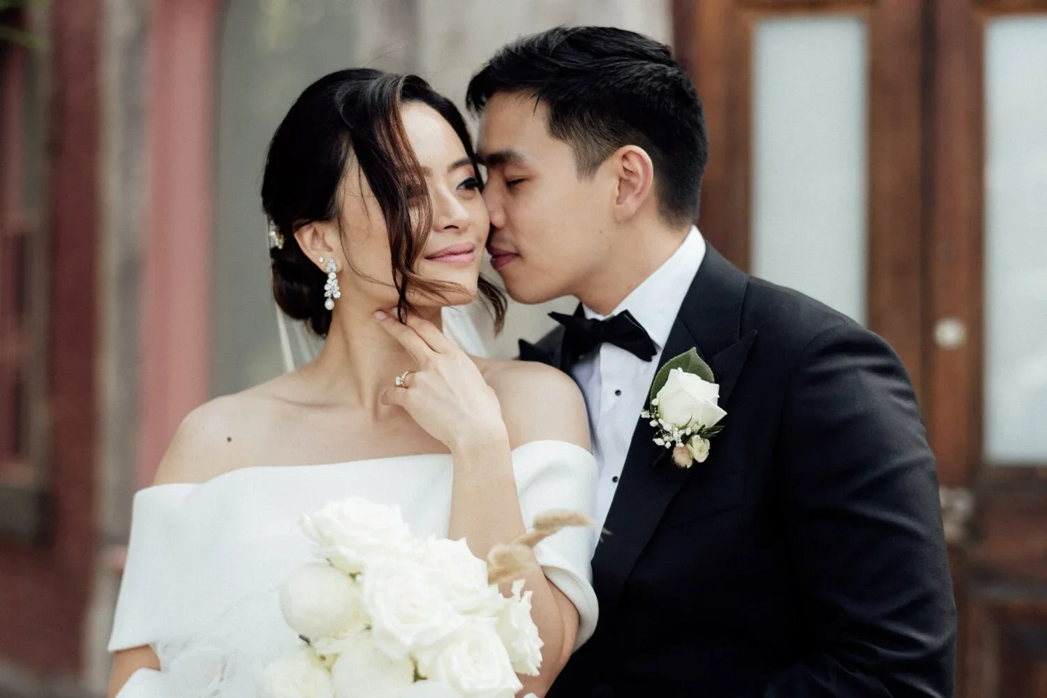 A bride and groom sharing a tender moment, dressed in wedding attire, with the groom whispering to the bride in an intimate pose.