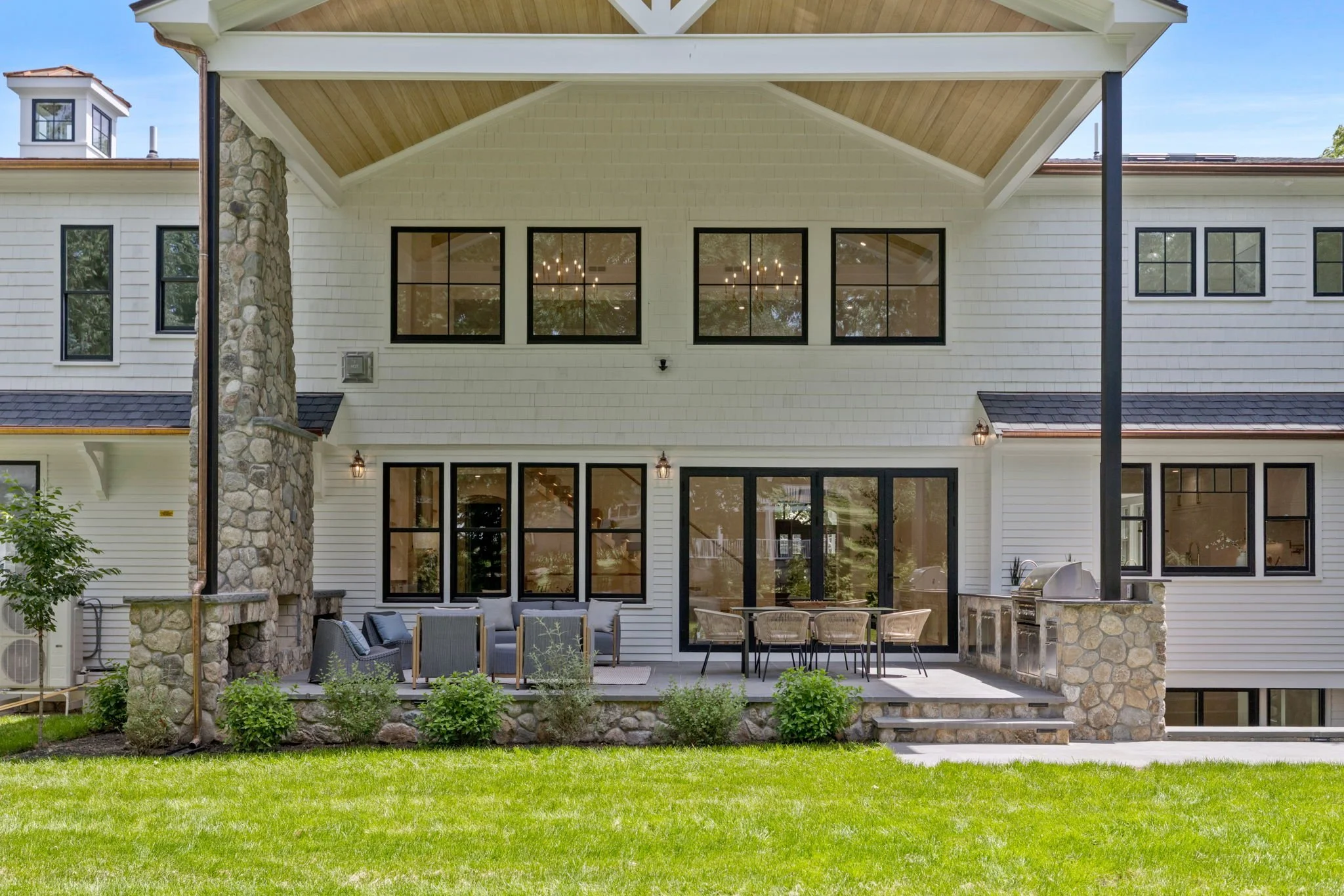 Backyard outdoor patio with seating area, stone and white siding house, large windows, and a lawn.