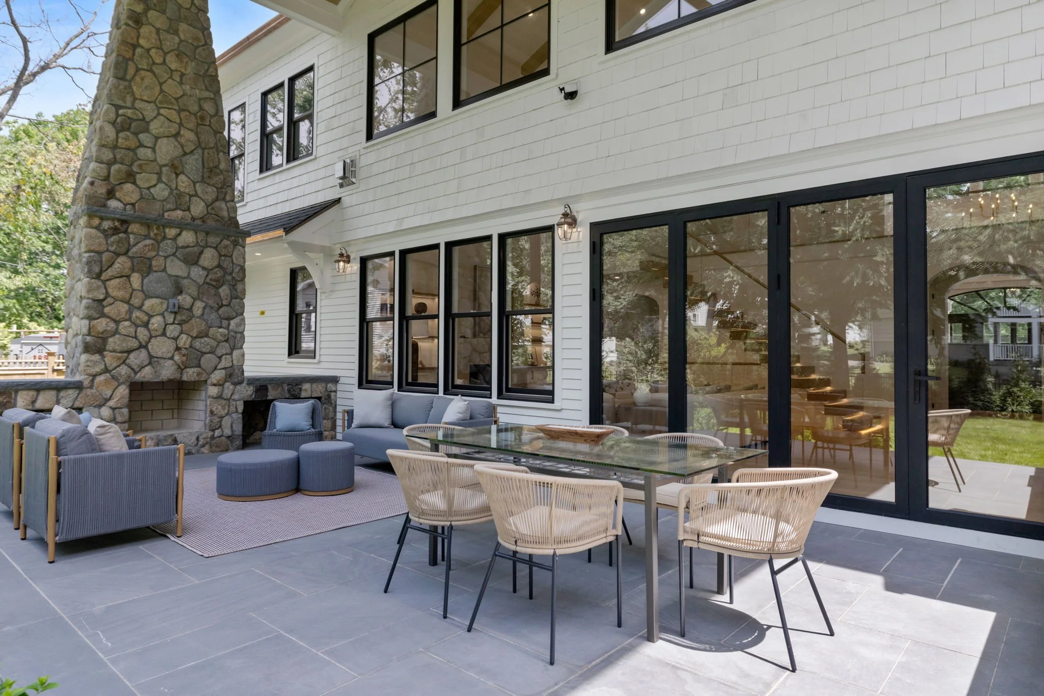 Backyard patio with outdoor seating, a stone fireplace, and large glass sliding doors leading into the house