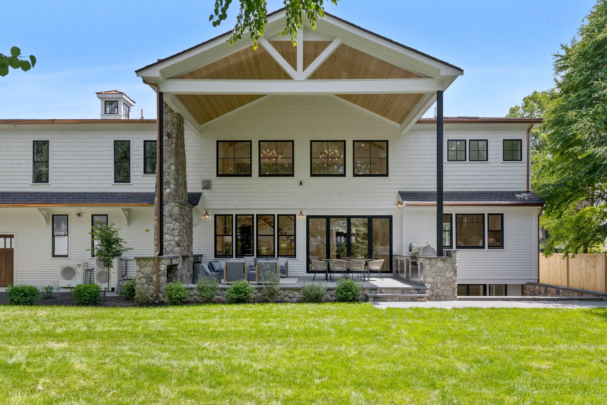 Back view of a modern white house with a large covered patio, outdoor furniture, and a green lawn.