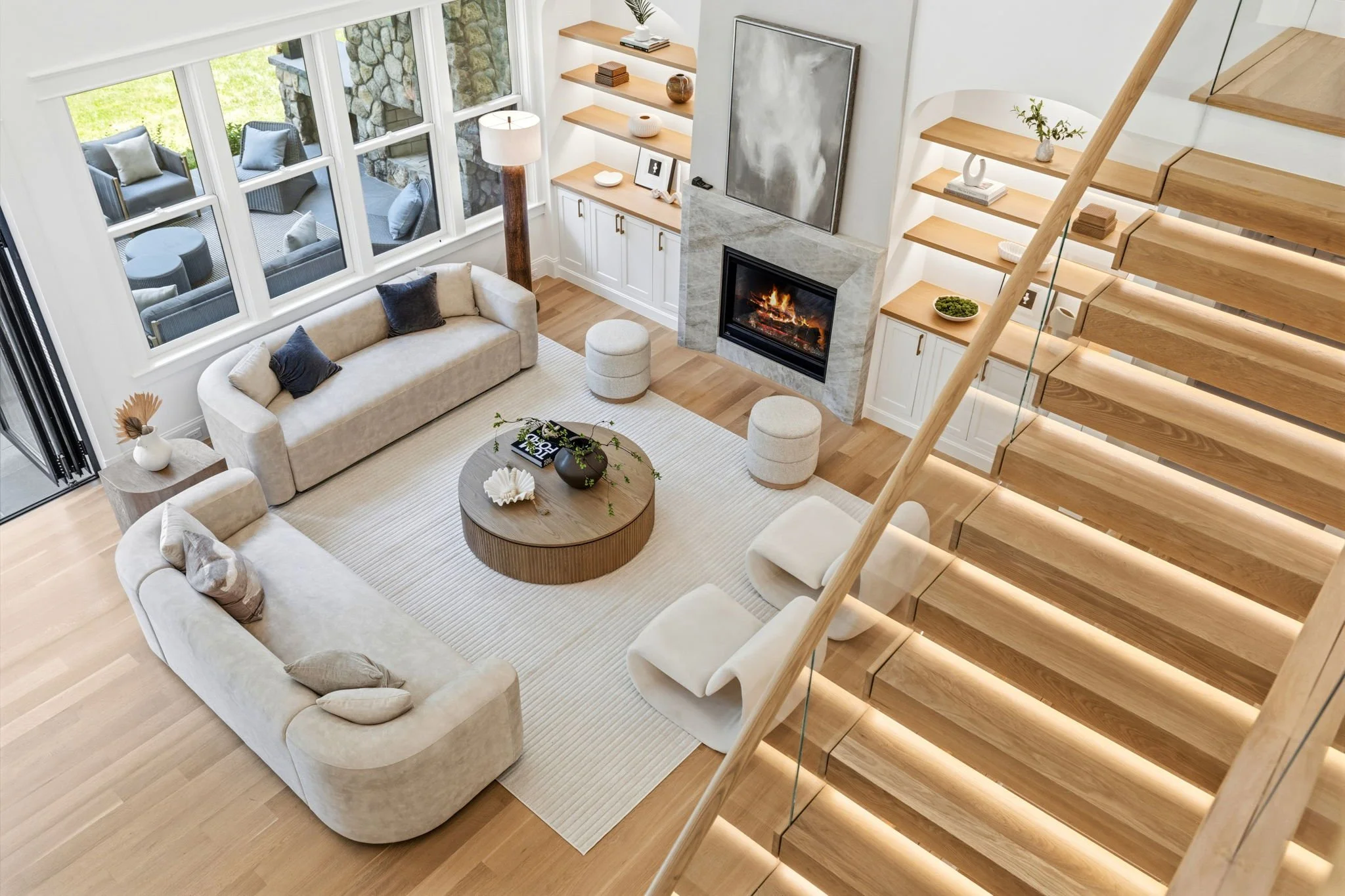 Living room with beige sofas, a white rug, a coffee table, a fireplace, and wooden stairs with glass railing.