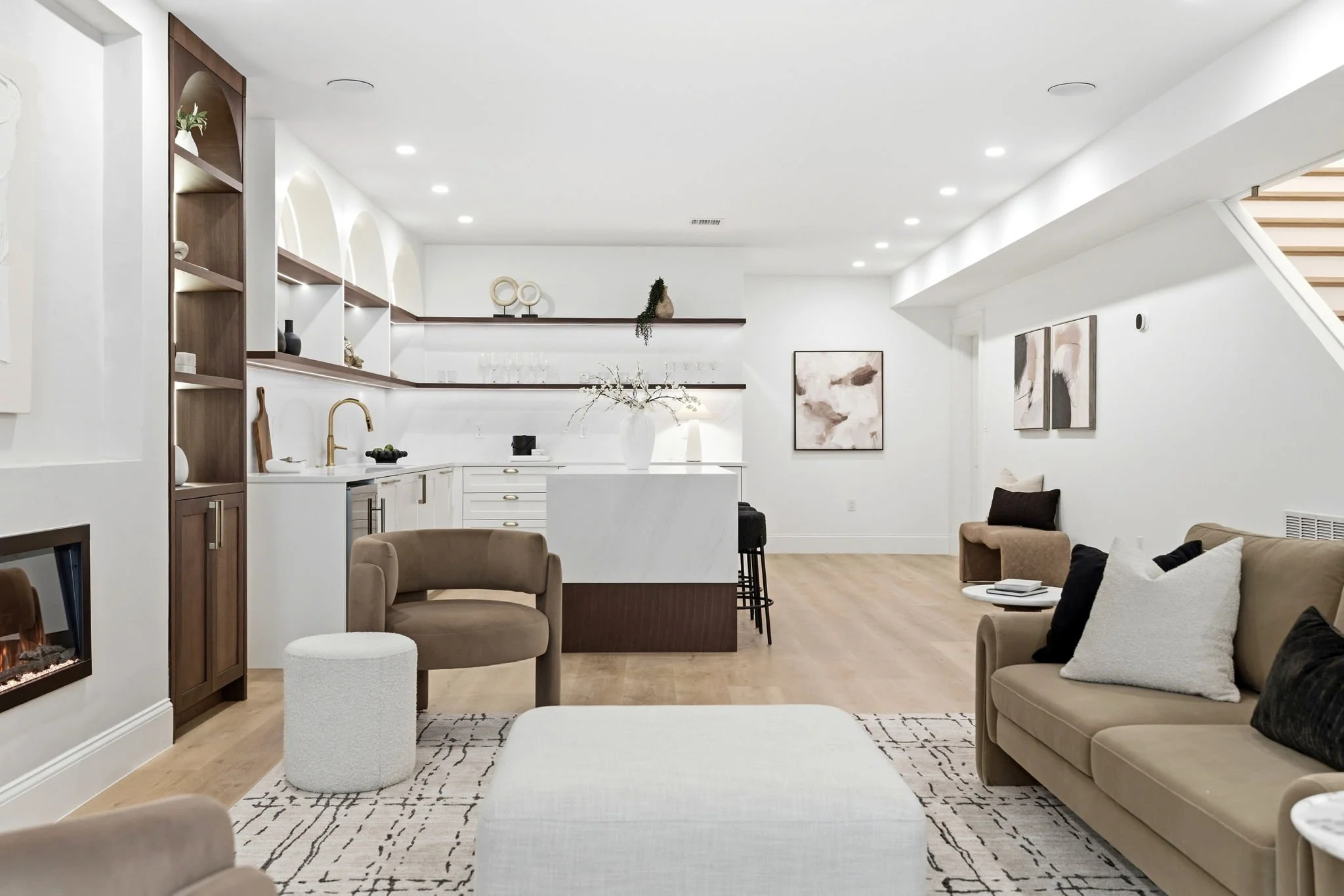 A modern open-concept living room and kitchen with white walls, wooden accents, and minimalist decor, including artwork and plants.