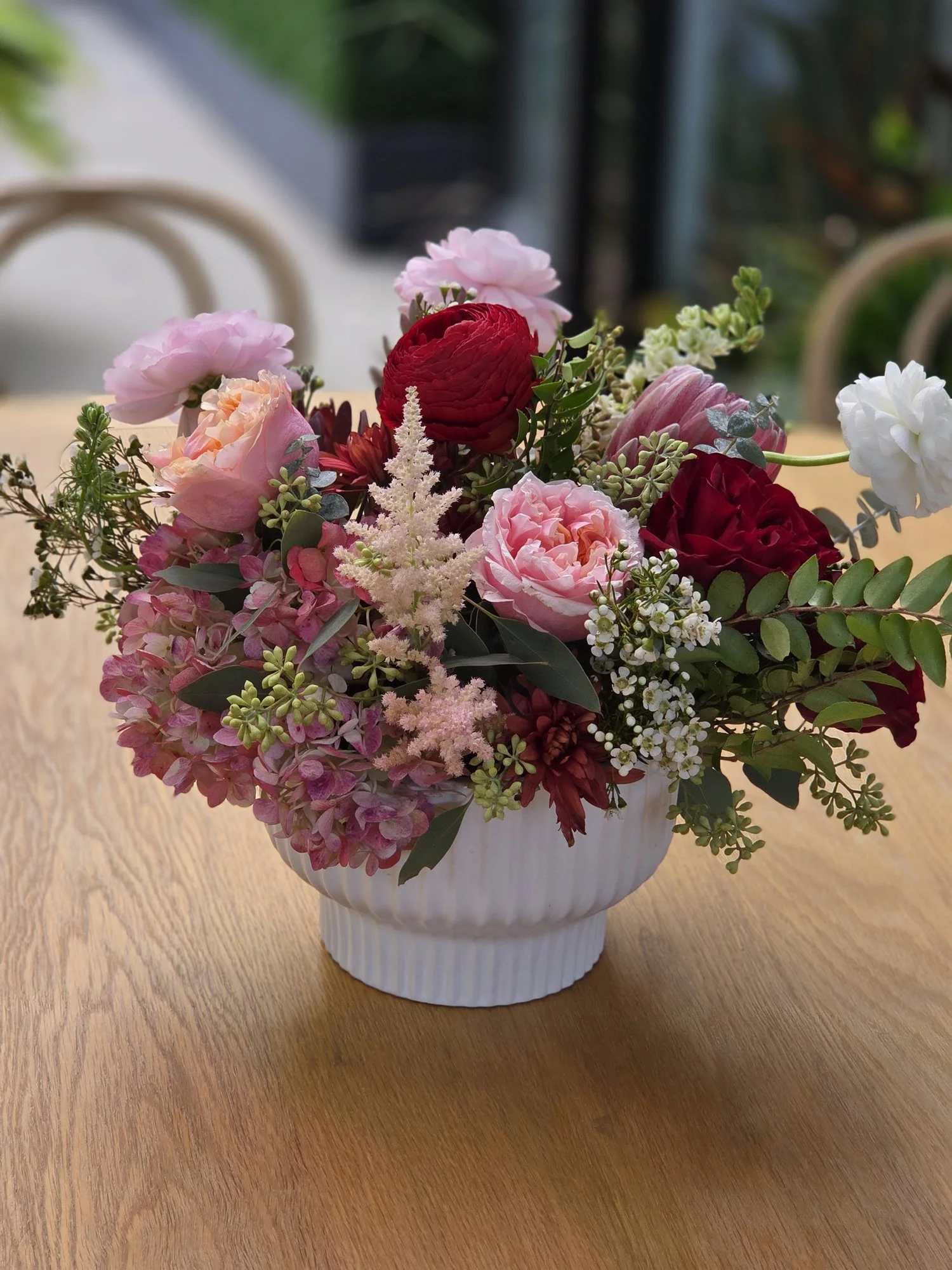Red and pink floral centerpiece in a white ribbed vase