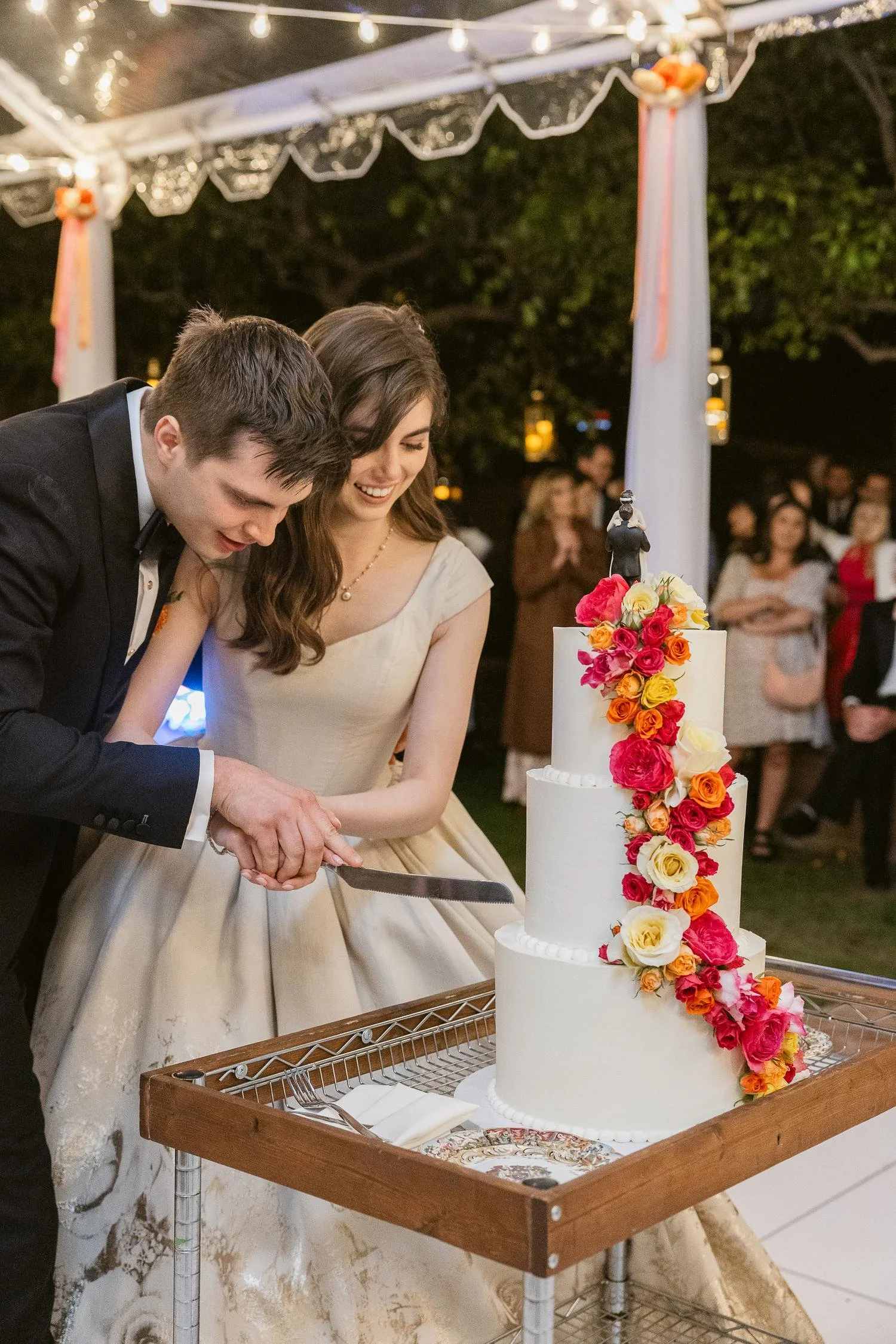 Bride and groom cutting 3-tiered white cake with bright floral cascade