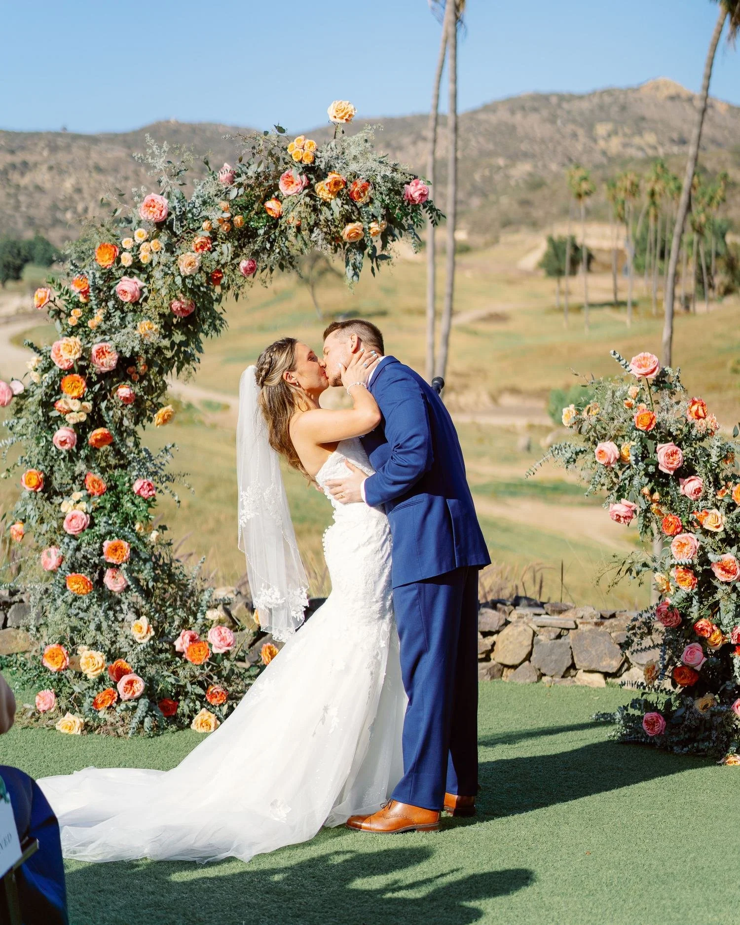 San Diego bride and groom's first kiss under colorful curved floral arch