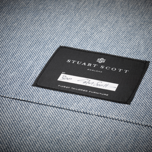 Close-up of a Stuart Scott furniture tag sewn onto a blue textured fabric.