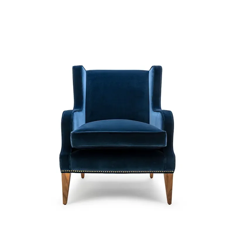A blue velvet armchair with wooden legs and gold nailhead trim, photographed against a white background.