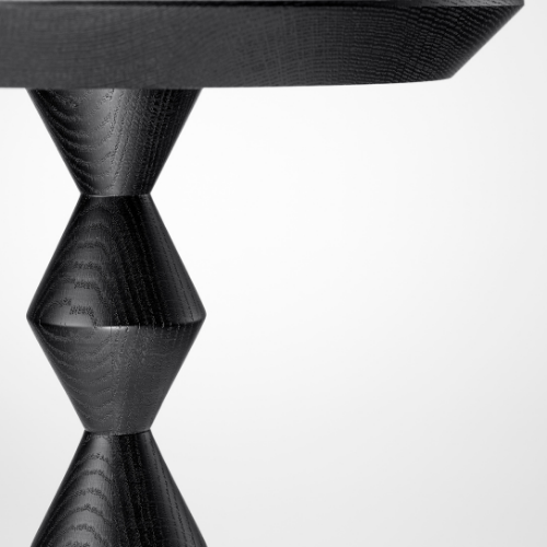 Close-up of a black wooden table leg with a geometric design against a white background.