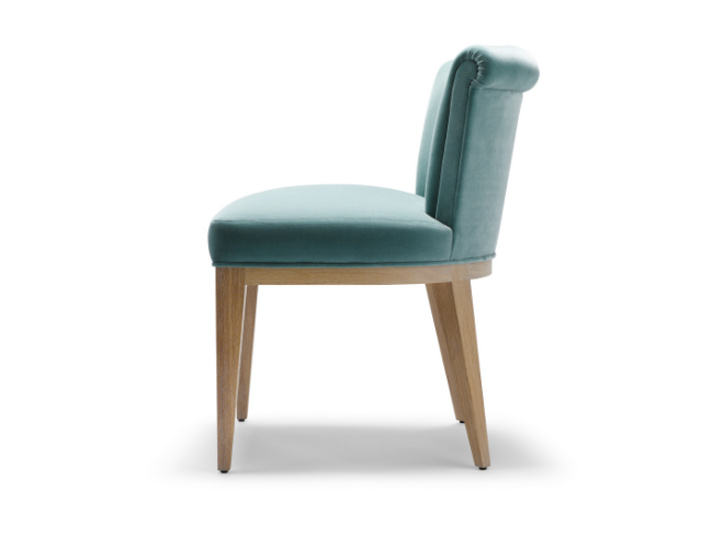 Side view of a modern upholstered chair with light wood legs, teal fabric, and a rounded backrest.