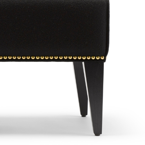 Close-up of black upholstered furniture leg with gold nailhead trim.