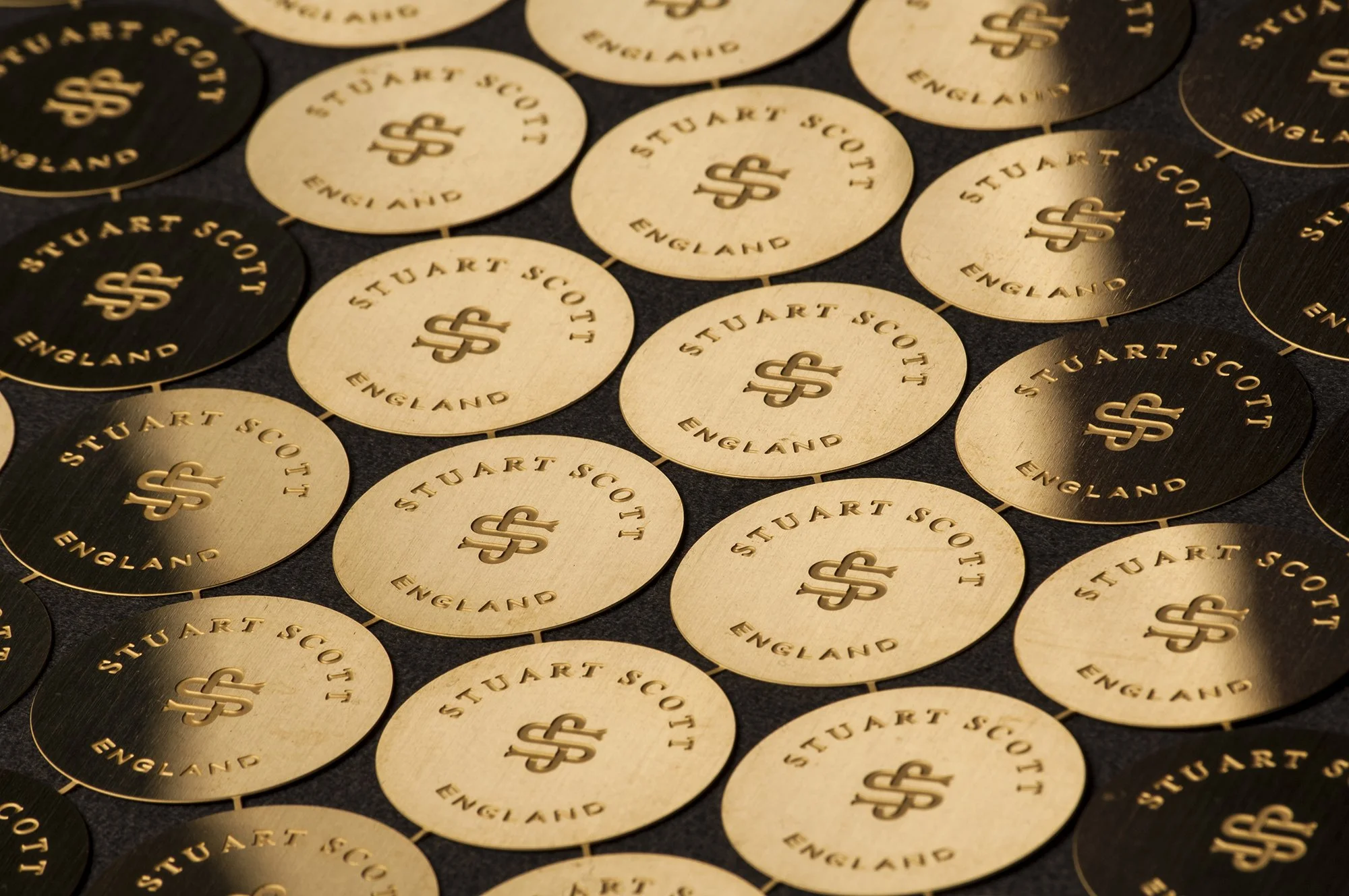 Close-up of multiple gold and black circular stickers featuring the text 'Stuart Scott England' and a dollar sign logo.