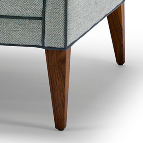 Close-up of a piece of furniture showing two wooden tapered legs and the corner of blue and gray fabric upholstery.