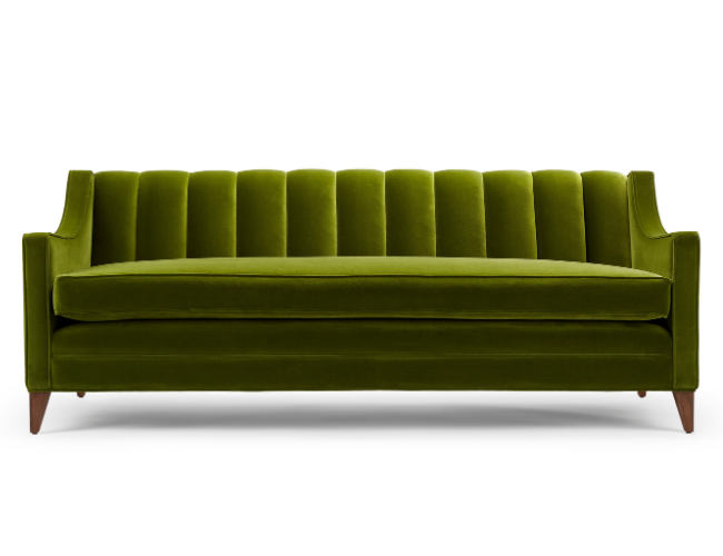 Green velvet sofa with tall, vertical tufted backrest and wooden legs.