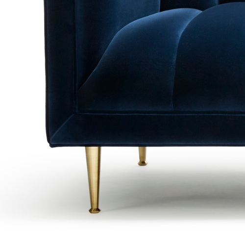 Close-up of a navy blue velvet armchair with gold tapered legs.
