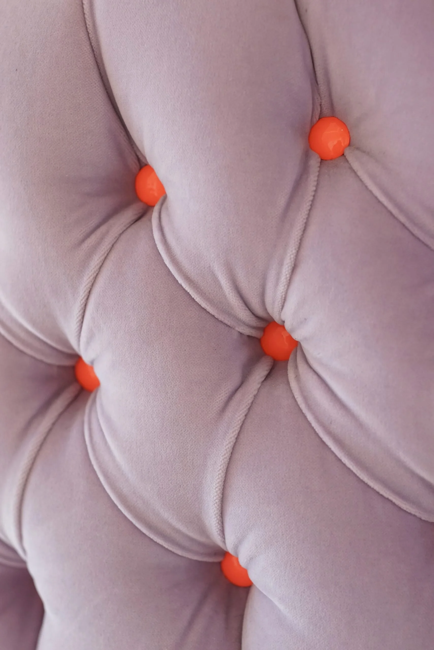 Close-up of a tufted, light pink fabric upholstery with orange decorative buttons.