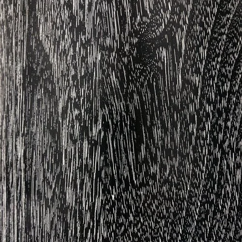 Close-up of a black surface with streaks of water, showing a reflection of a person taking a photograph.