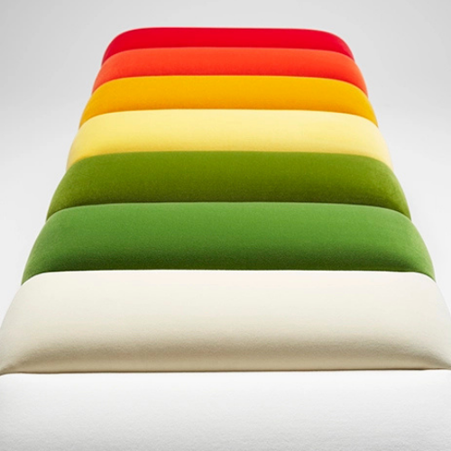 Stack of colorful upholstered cushions in red, orange, yellow, light yellow, green, dark green, and white arranged in a tiered formation.