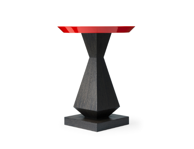 A modern side table with a black geometric wooden base and a round red tabletop.