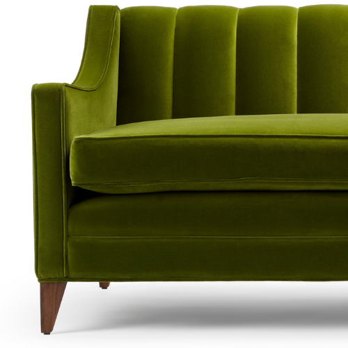 Close-up of a green velvet sofa with wooden legs.