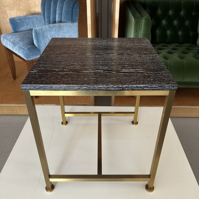 A modern side table with a dark wood top and gold metal frame, placed on a white surface.