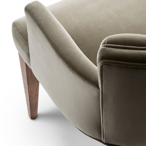 Close-up of a modern upholstered armchair with wooden legs, beige fabric, curved armrest, and plush cushioning.
