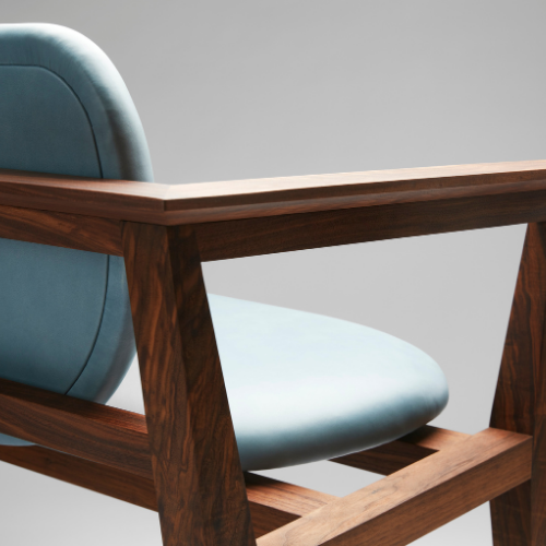 Close-up of a wooden chair with a light blue cushion, featuring a curved backrest, against a plain light gray wall.