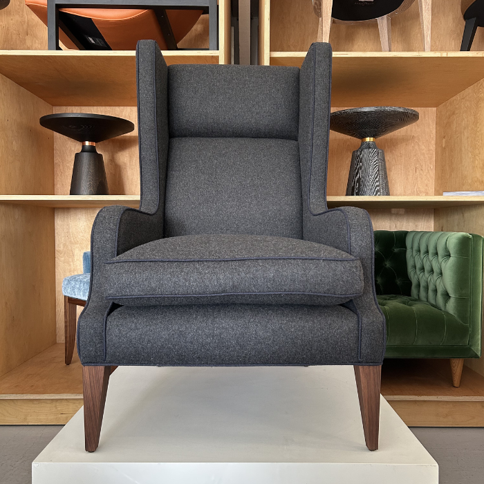 A dark gray upholstered armchair with a high back and wooden legs, positioned on a white platform in a furniture store.