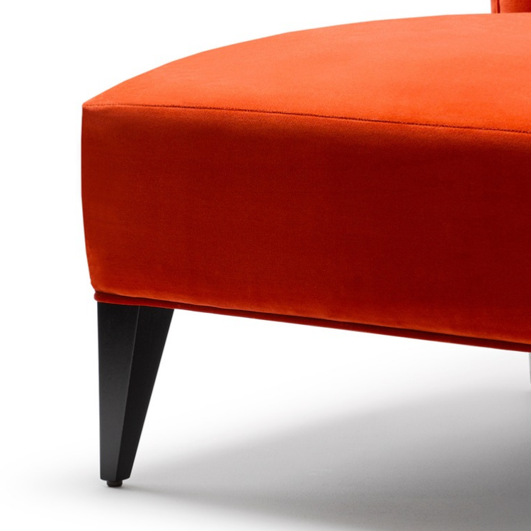 Close-up of an orange upholstered chair with black tapered legs.