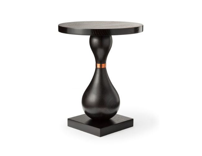 A black wooden side table with a round top and a sculptural base, featuring a small copper ring around the narrow part of the base.