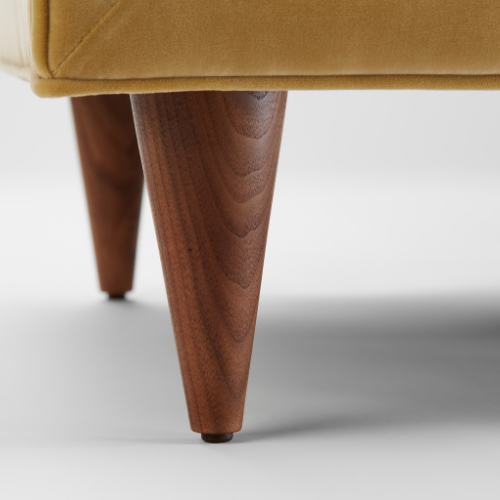 Close-up of a wooden furniture leg supporting a mustard-colored upholstered piece.
