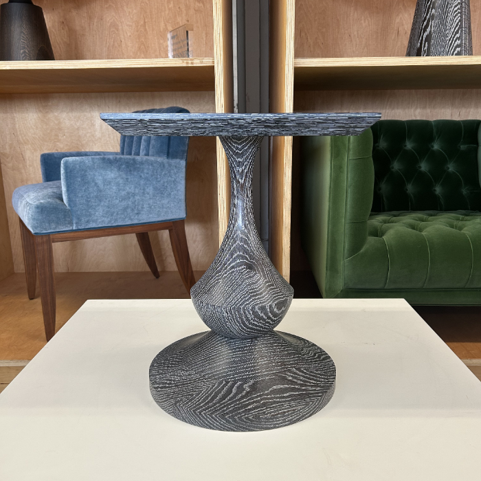 A modern black wooden side table with a rounded base and a flat circular top, placed on a white surface in a furniture store.